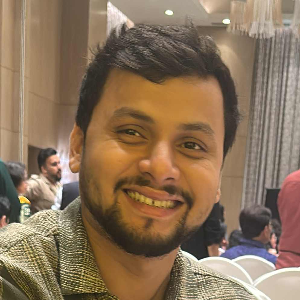 Man sitting on a chair in a formal event setting with people and decorations in the background